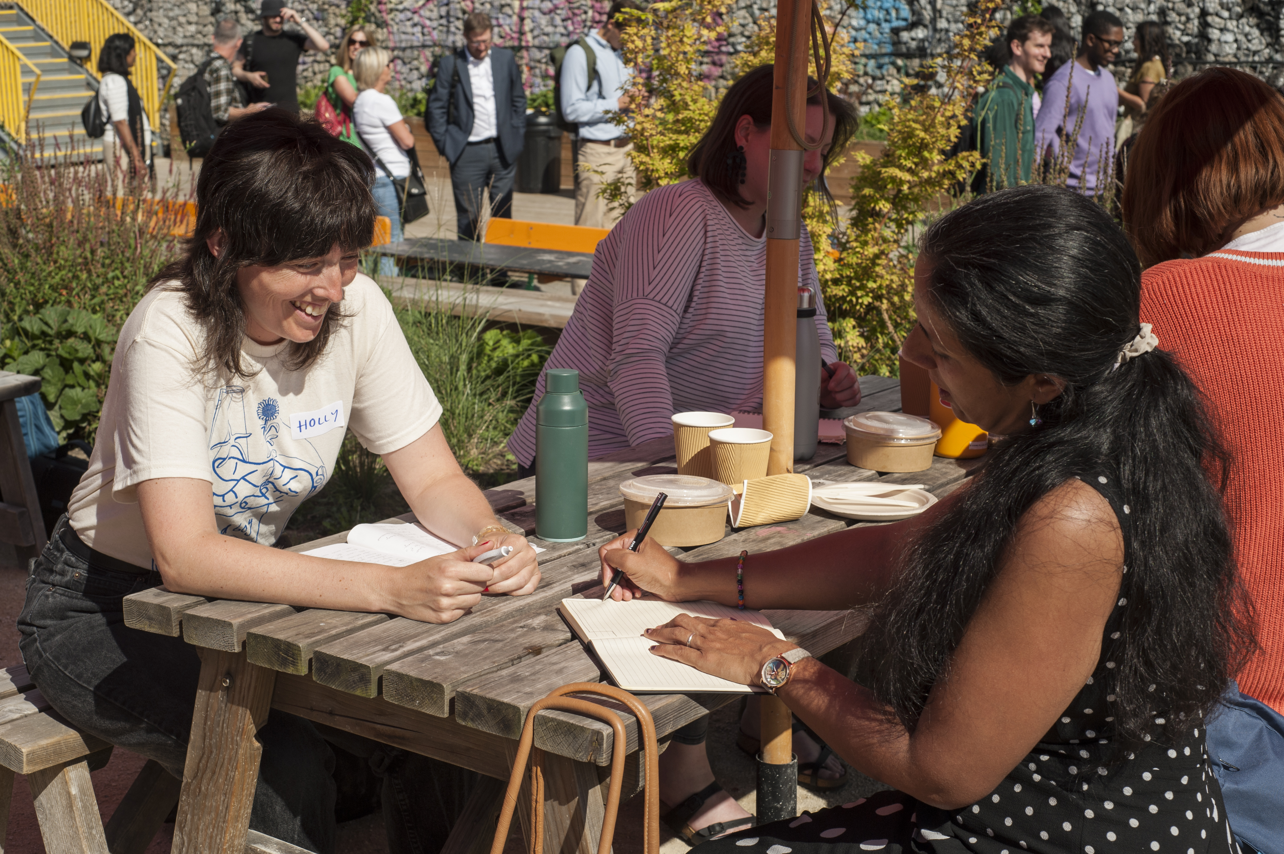 Two people sitting on a bench outside in the sun, smiling and talking